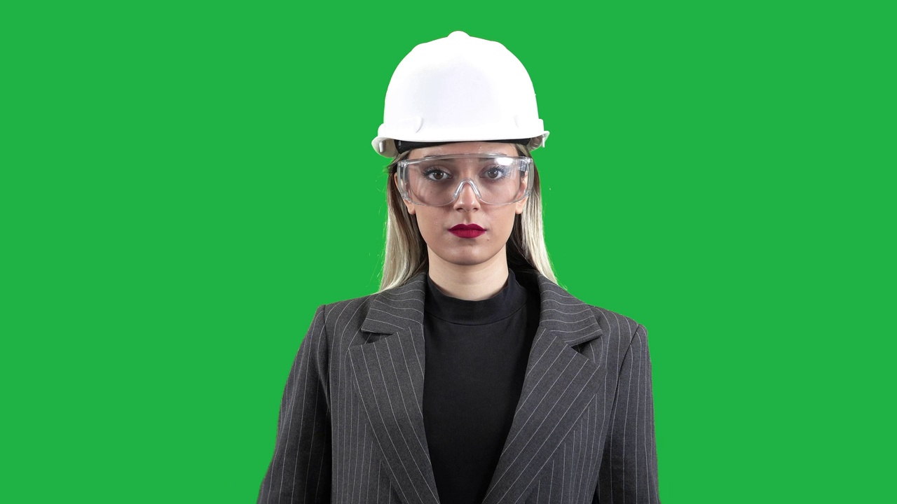 穿着防护服的女建筑师使用数字平板电脑，年轻的女工程师拿着平板电脑站在绿屏上看周围的物体，色度键。视频下载