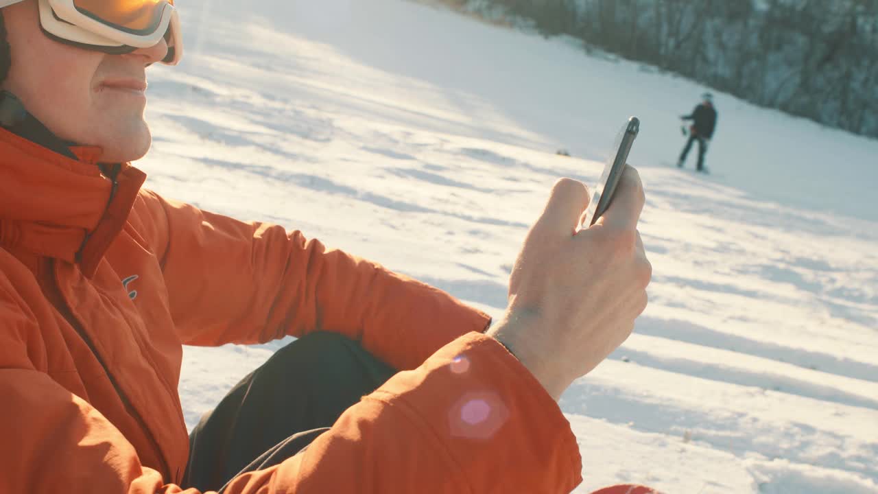 戴着滑雪护目镜的男子一边用手机打字一边滑雪特写视频下载