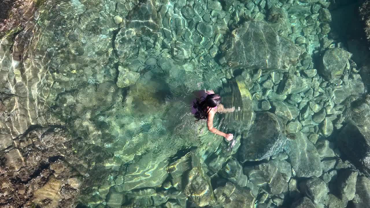 一个小游泳池，沿着海洋被火山岩包围，是一个穿着泳衣的模特放松的宁静环境。视频素材