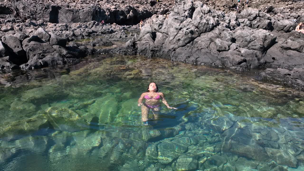从空中的角度来看，一个穿着泳衣的容光焕发的女人躺在海边，享受着她的时光。视频下载