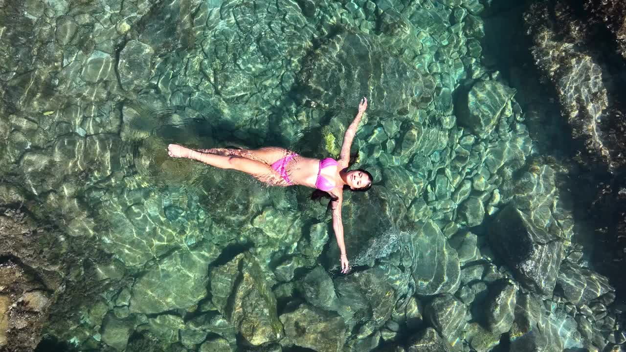 一名身穿泳衣的女模特在海边火山岩环绕的小水池里放松身体。视频下载