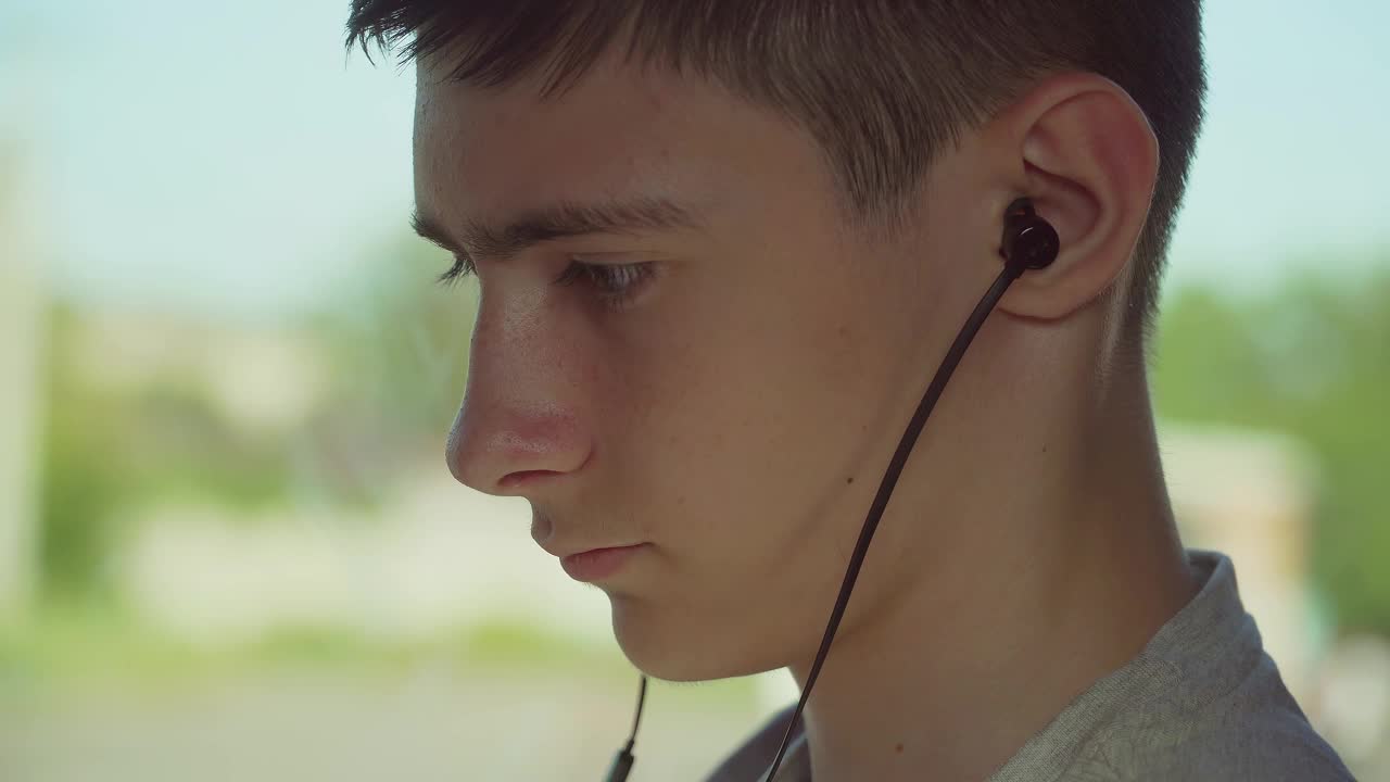 关闭了。图为一个十几岁的男孩坐在公共交通工具的窗户边，用智能手机通过有线耳机听音乐视频素材