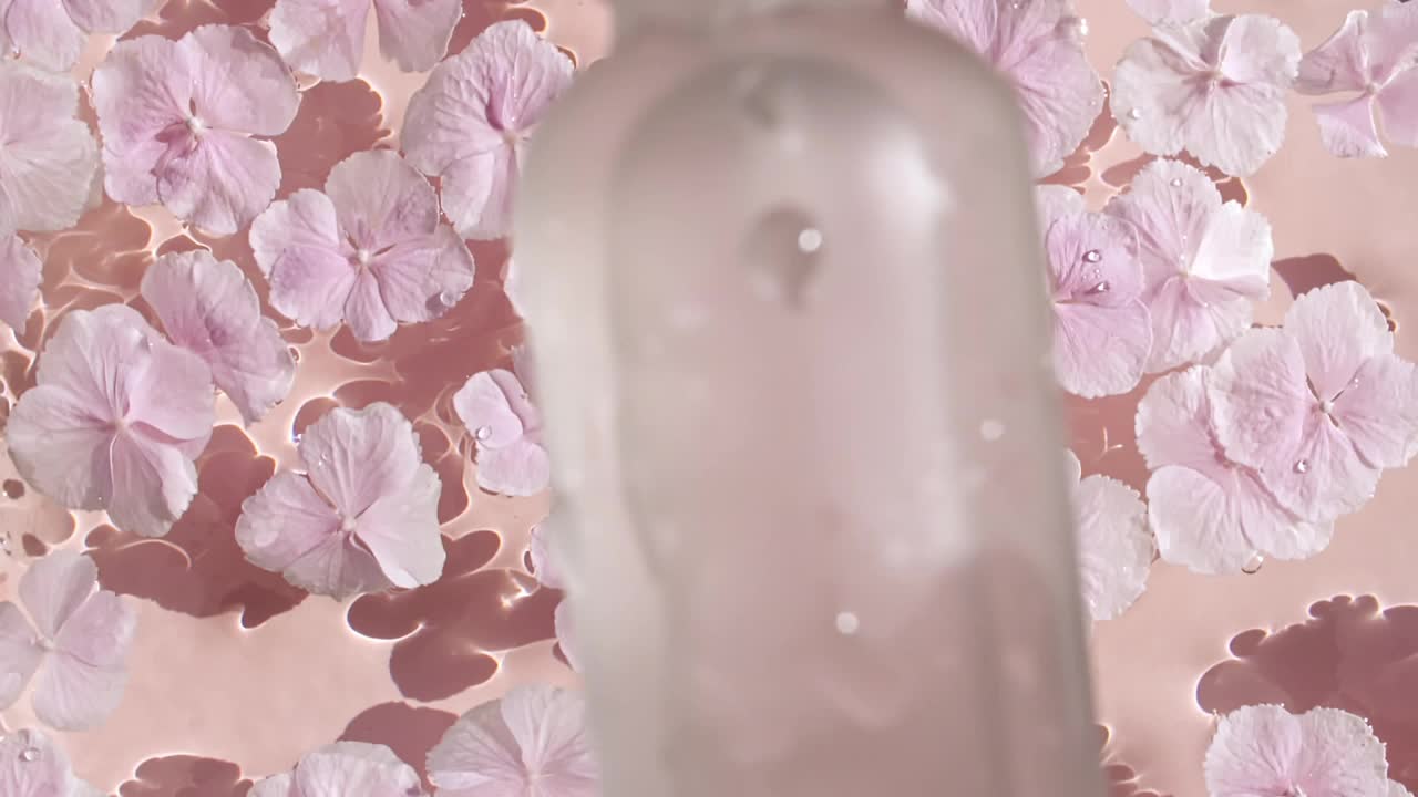 化妆品瓶，小瓶油，液体，胶原蛋白血清落在水和飞溅在粉红色的背景。缓慢的运动。女性化妆品护肤品。美容产品包装布局样图。视频下载