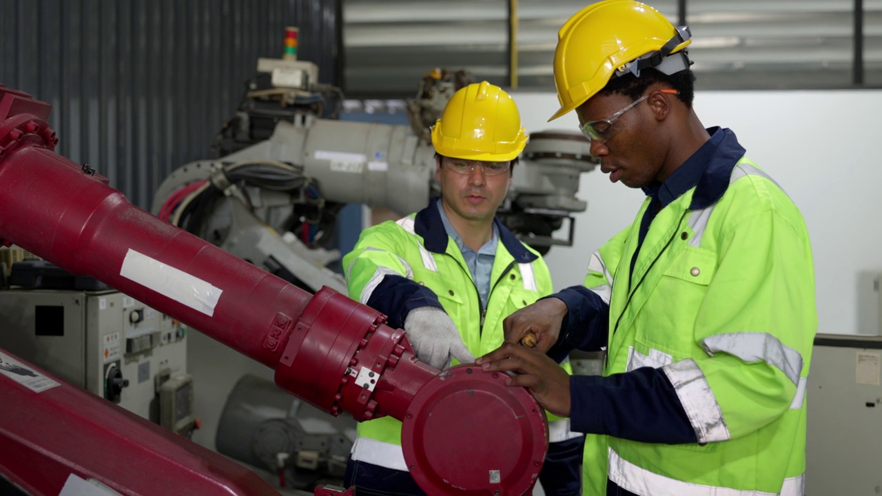 非裔美国工程师、白人技术员在焊接工厂用螺丝刀检查机器人机械臂。视频素材