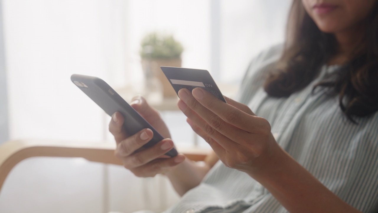 的手。亚洲女性正在用信用卡、智能手机进行网上购物，在家进行网上交易或金融视频下载