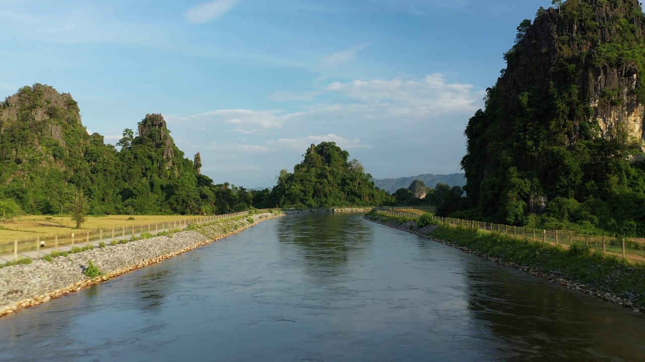 在一个阳光明媚的日子里，一条被稻田和喀斯特山峰环绕的运河，在老挝的哈穆内，朝向他克。视频下载