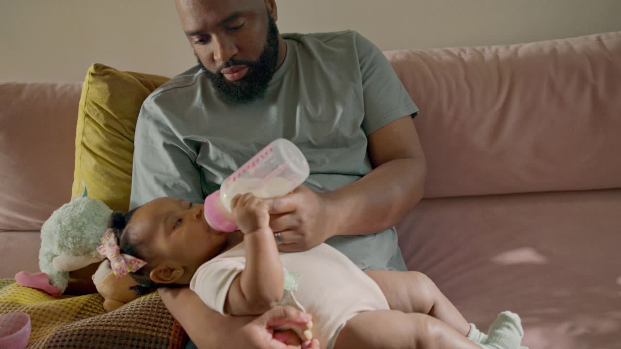 慈爱的爸爸和他好奇的小宝贝在舒适的沙发上享受安静的奶瓶喂养视频下载