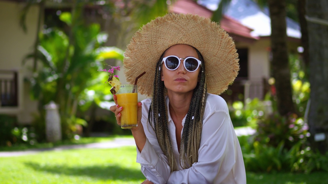 肖像女游客享受夏日冷饮香蕉鲜榨果汁，暑假休息。戴着太阳镜和帽子的女人在夏天喝橙汁。度假的概念视频下载