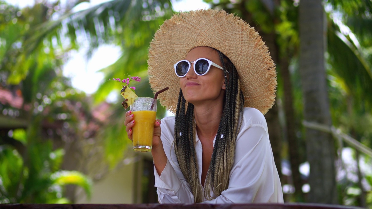 特写:年轻快乐的女游客戴着太阳镜和帽子，喝着橙汁，享受着夏日的奢华假期。一名女游客在当地的户外咖啡馆里休息视频下载