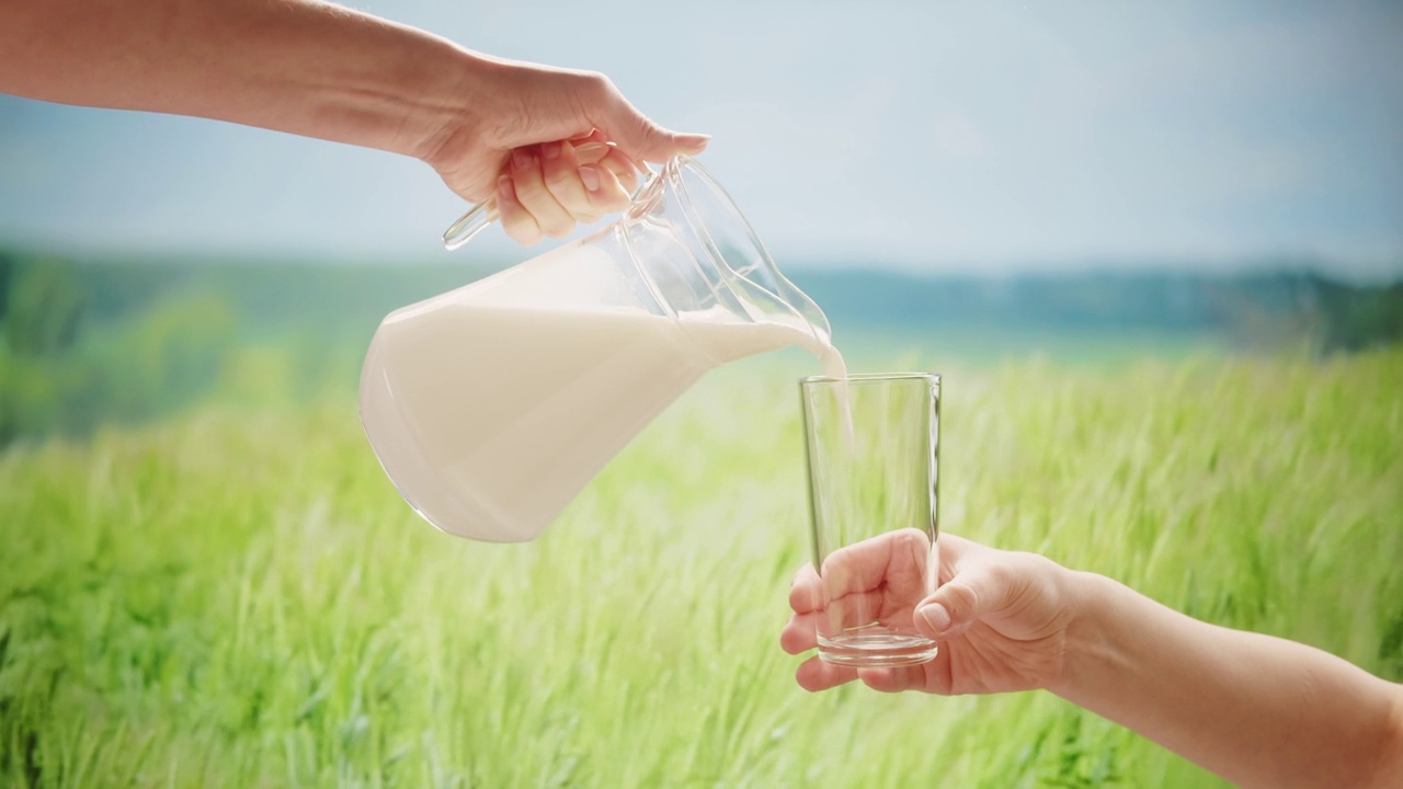 牛奶从罐子里倒进玻璃杯里，在田野前，草地为背景视频下载