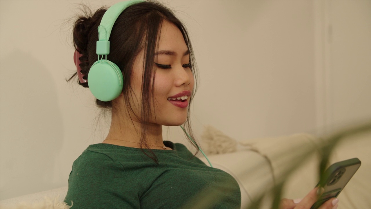 年轻女子在家里戴着耳机放松。视频下载