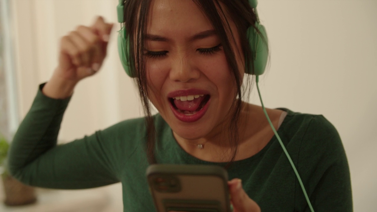 戴着耳机的年轻女子在家里唱歌跳舞。视频下载