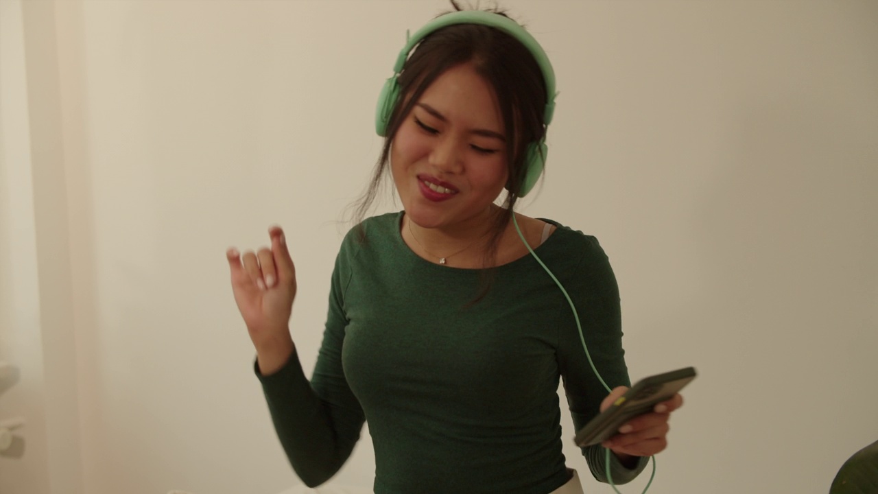 戴着耳机的年轻女子在家里唱歌跳舞。视频下载