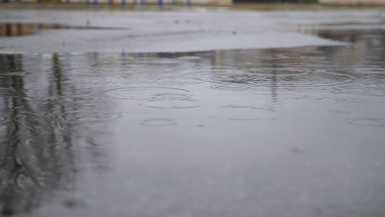 小雨滴落在柏油路上的大水坑里。雨滴溅落在反光的水面上。春季或秋季雨季。宁静场景的概念。慢动作视频下载