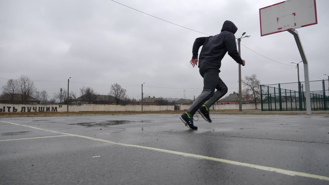 健壮的男运动员在雨中沥青路场上训练飞梭。穿着运动服的运动员在阴天锻炼。在户外运动的年轻运动员。健康积极生活方式的理念视频下载