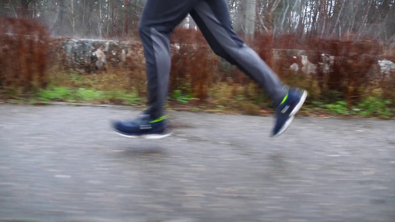 年轻运动员在下雨天沿着小路奔跑的双腿。男运动员沿着柏油路慢跑的脚。强壮、耐力强的户外训练运动员。积极生活方式的概念。近距离视频下载