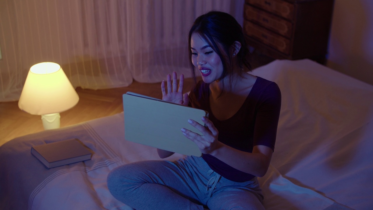 一个微笑的年轻女子躺在床上拿着平板电脑的肖像。视频下载