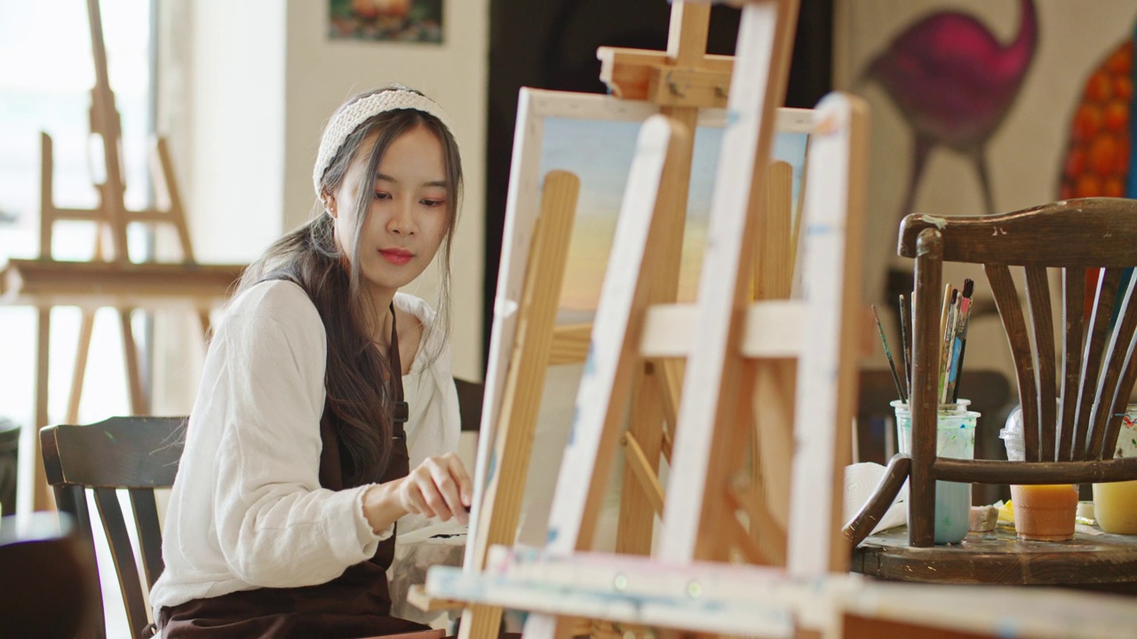 年轻的亚洲女艺术家在艺术工作室画日落风景画。视频下载