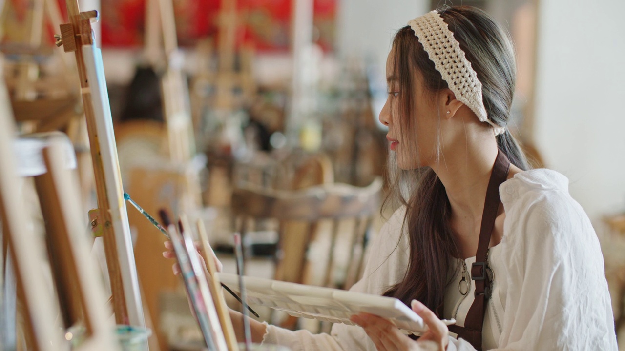 年轻的亚洲女艺术家在艺术工作室画日落风景画。视频下载
