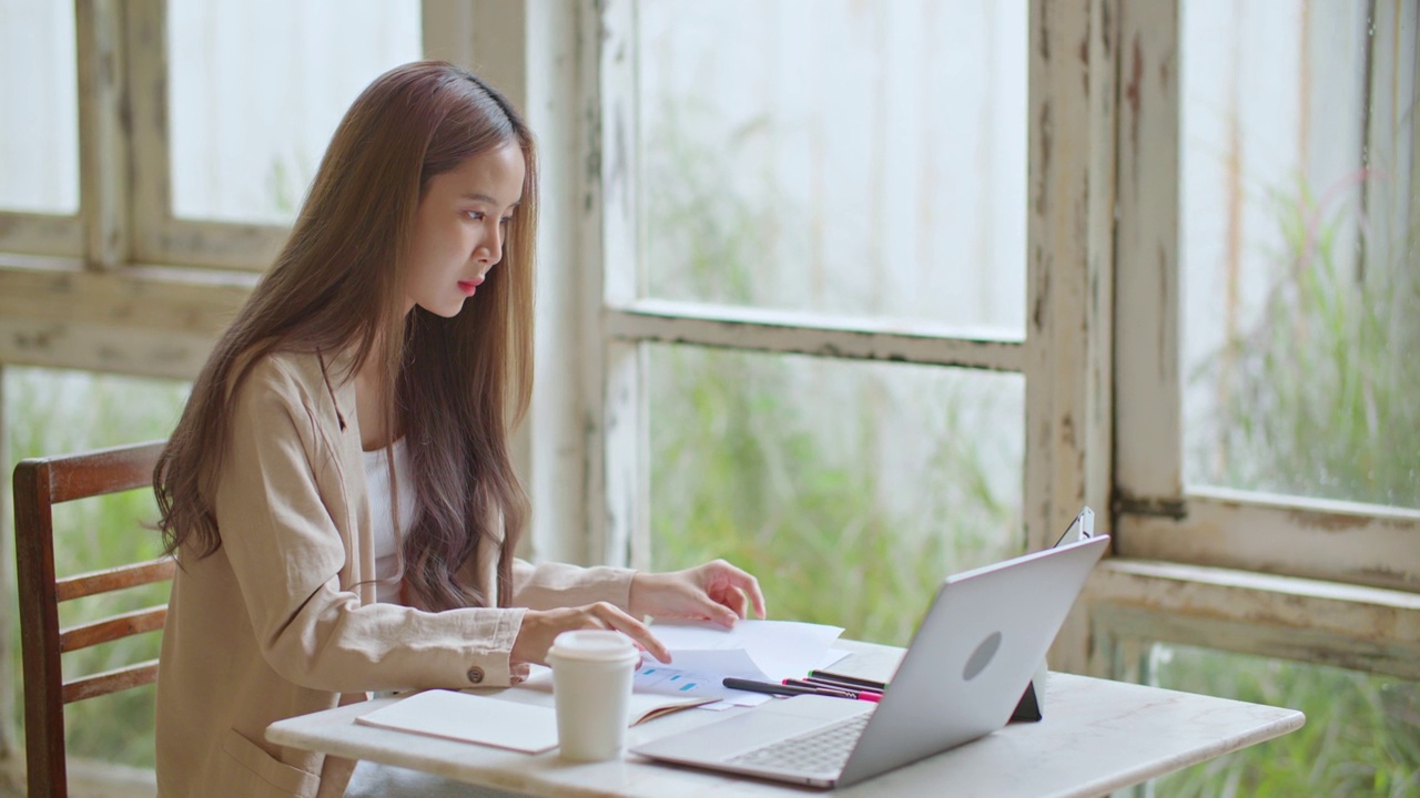 亚洲女性自由职业者使用笔记本电脑远程工作在共同工作空间咖啡馆。视频下载