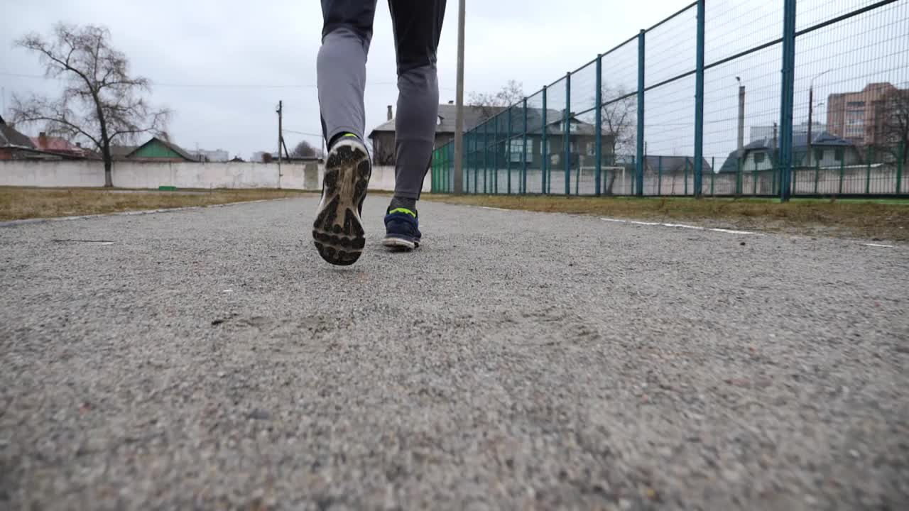 男运动员的脚在学校体育馆的小路上慢跑。年轻运动员在田径场上奔跑的双腿。强壮、耐力强的户外训练运动员。积极生活方式概念视频下载