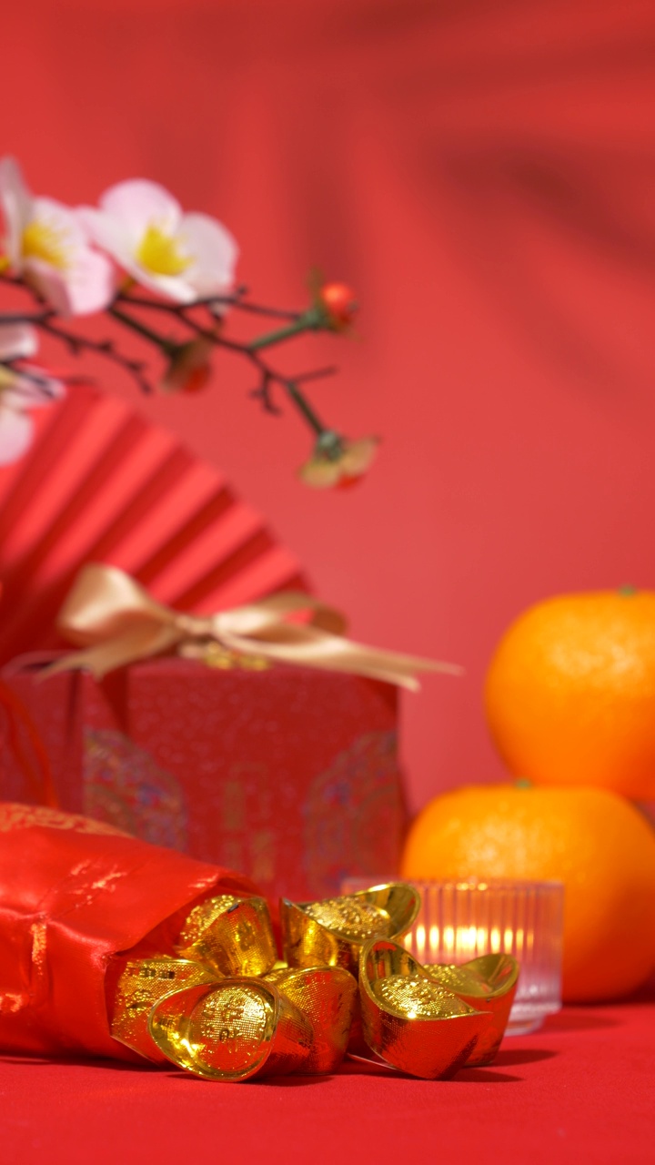 中国农历新年的背景。中国古代金条在丝绸袋，红色礼盒与金弓，纸扇，橘子，梅花枝，蜡烛和树叶的影子摇摆。垂直视频下载