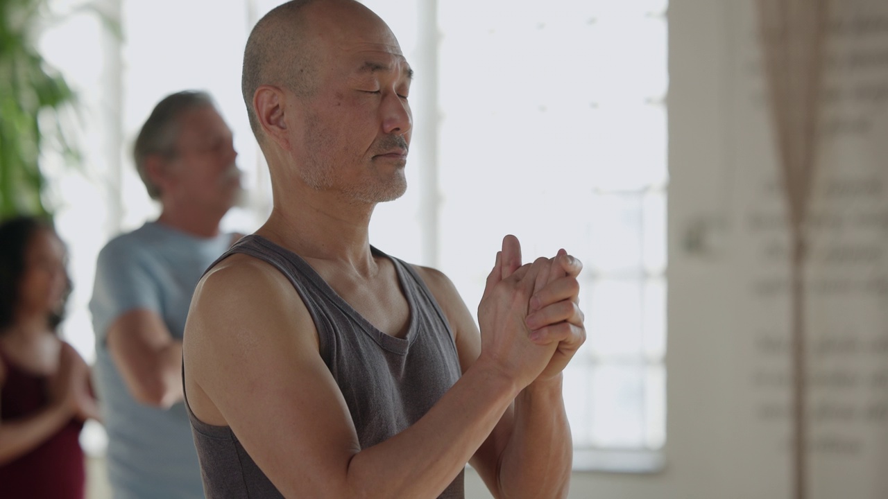 一名亚洲男子在瑜伽课上冥想，双手放在胸前视频下载