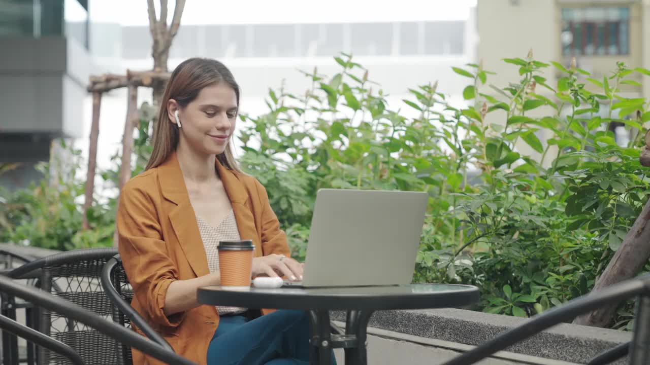在户外咖啡馆旅行时，女商人喝着咖啡，用笔记本电脑进行在线会议视频下载