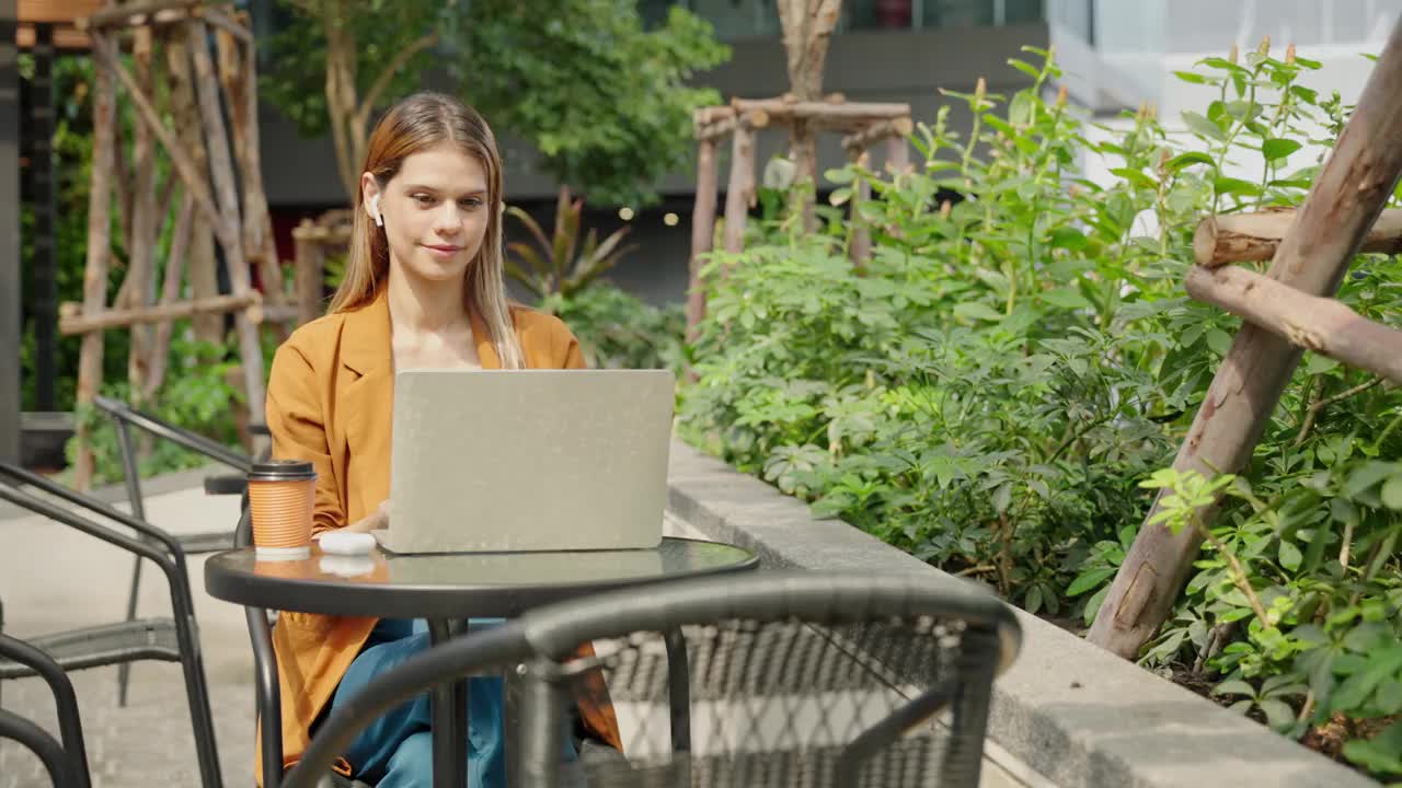 在户外咖啡馆旅行时，女商人喝着咖啡，用笔记本电脑进行在线会议视频下载