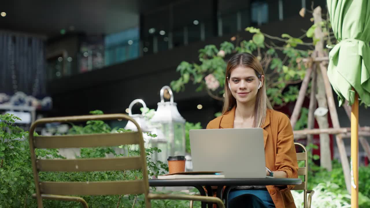 在户外咖啡馆旅行时，女商人喝着咖啡，用笔记本电脑进行在线会议视频素材