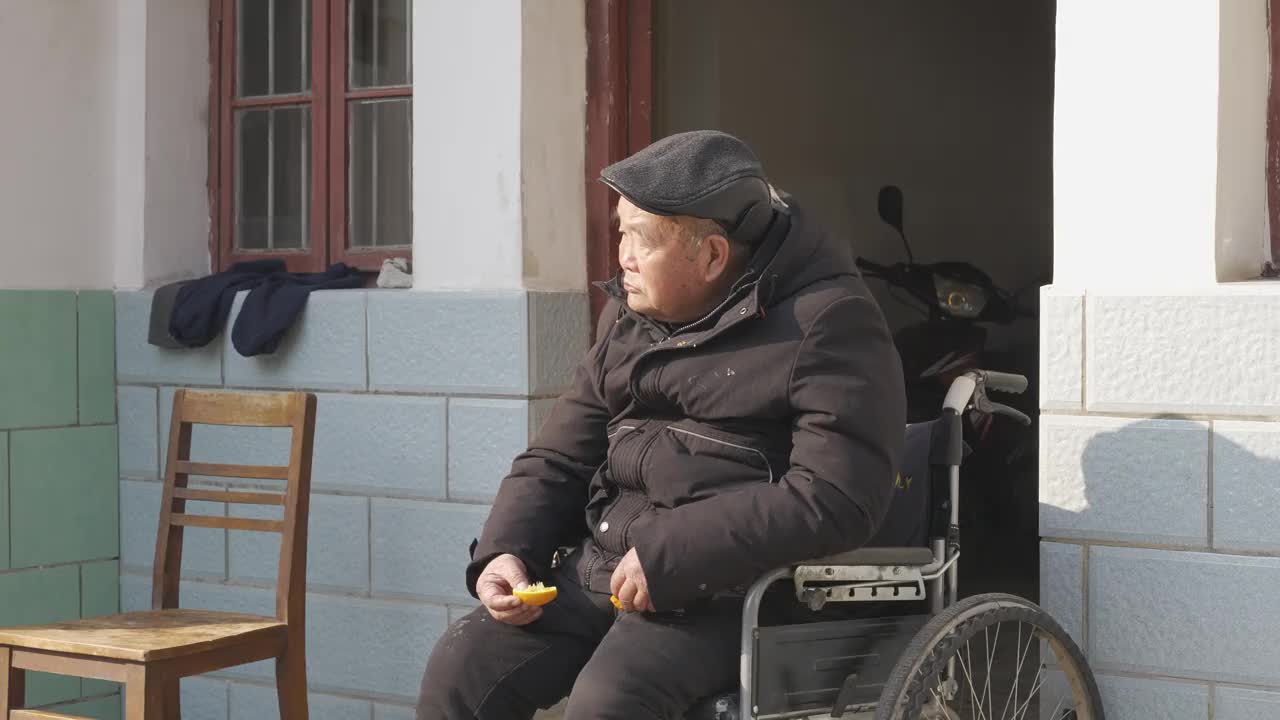 一位亚洲老人坐在自家门口，坐在轮椅上吃着水果，人口老龄化，老人养老问题视频素材
