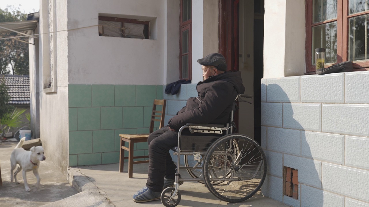 一位亚洲老人坐在自家门口的轮椅上，人口老龄化，老人护理问题视频素材