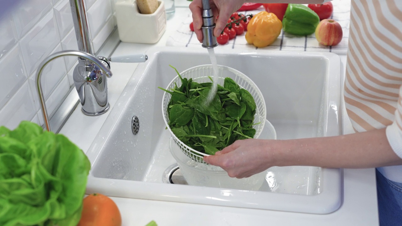 用滤器在厨房水槽的流水下手洗新鲜的菠菜叶。健康饮食。视频下载