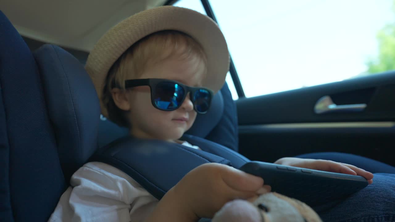 戴着太阳镜和帽子坐在汽车座椅上的小男孩视频下载