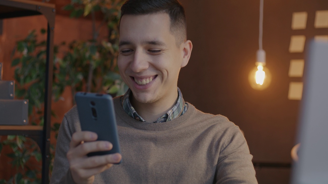 年轻的商人用信用卡和智能手机转账，晚上在办公室表达幸福视频素材