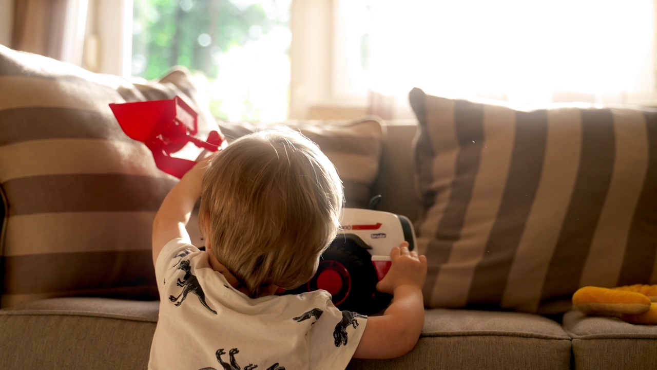 小男孩抱着红色玩具坐在沙发上视频下载