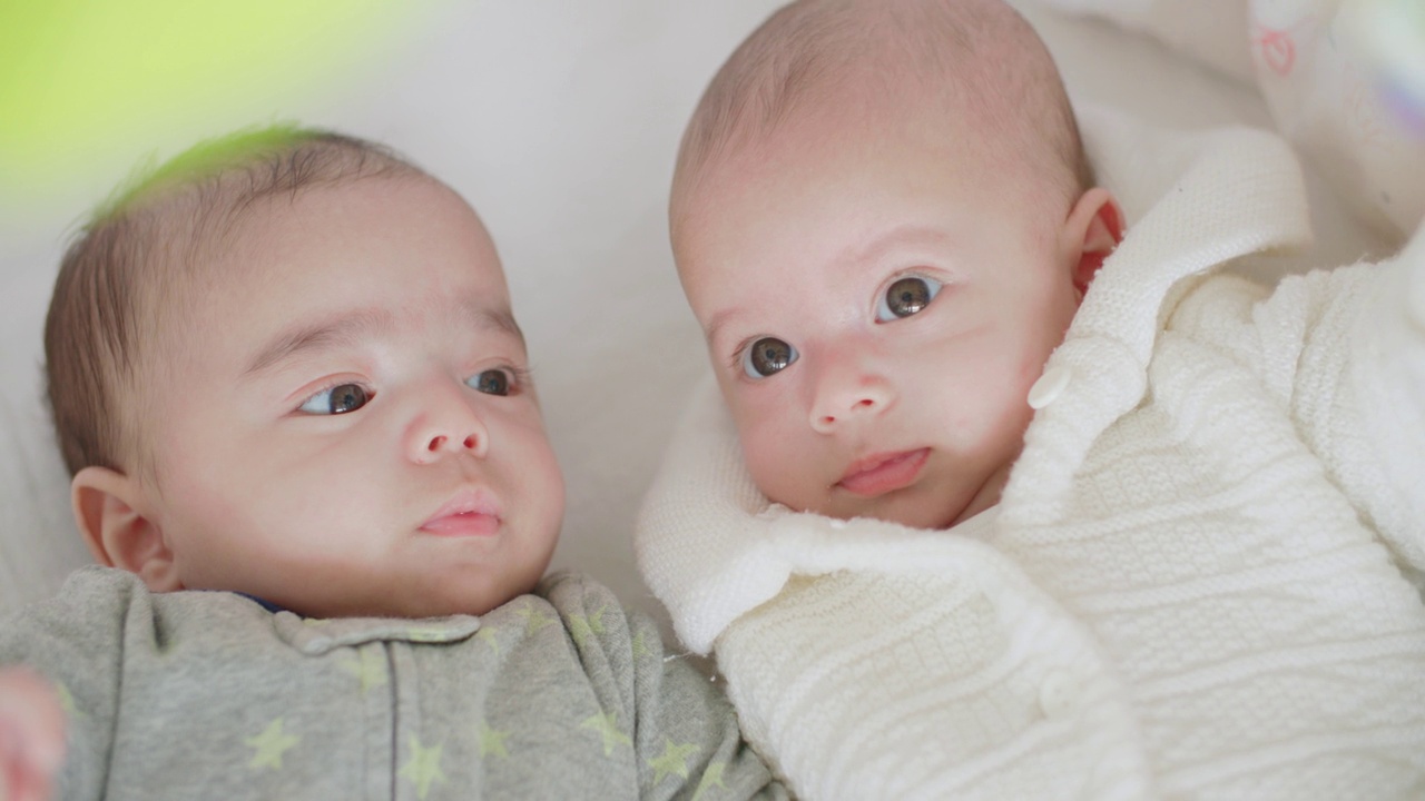 可爱的刚出生的双胞胎宝宝男孩和女孩一起躺在家里的床上。视频下载