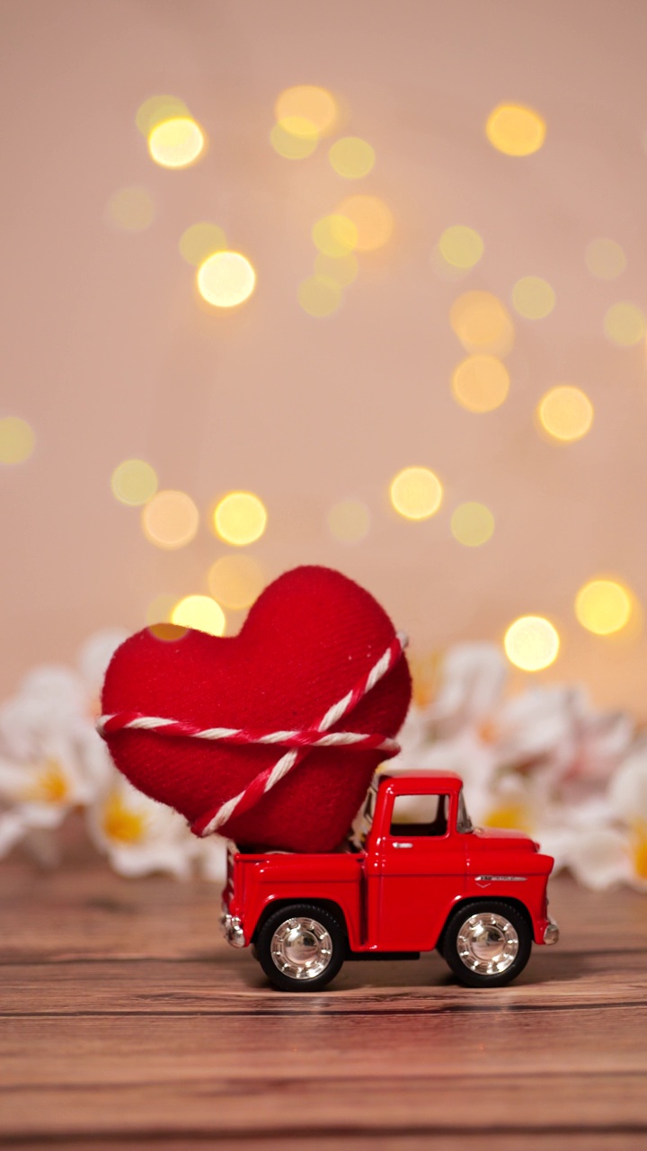 红色卡车，后面有一颗大红心，用来送情人节的爱，粉色背景，模糊的白色花田，散焦闪闪的散景光，垂直镜头视频下载