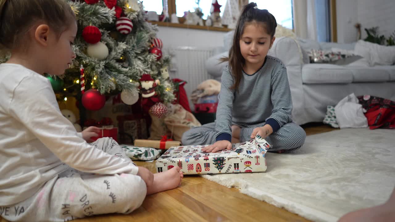 姐妹们穿着睡衣坐在圣诞树旁，打开她们的圣诞礼物视频下载