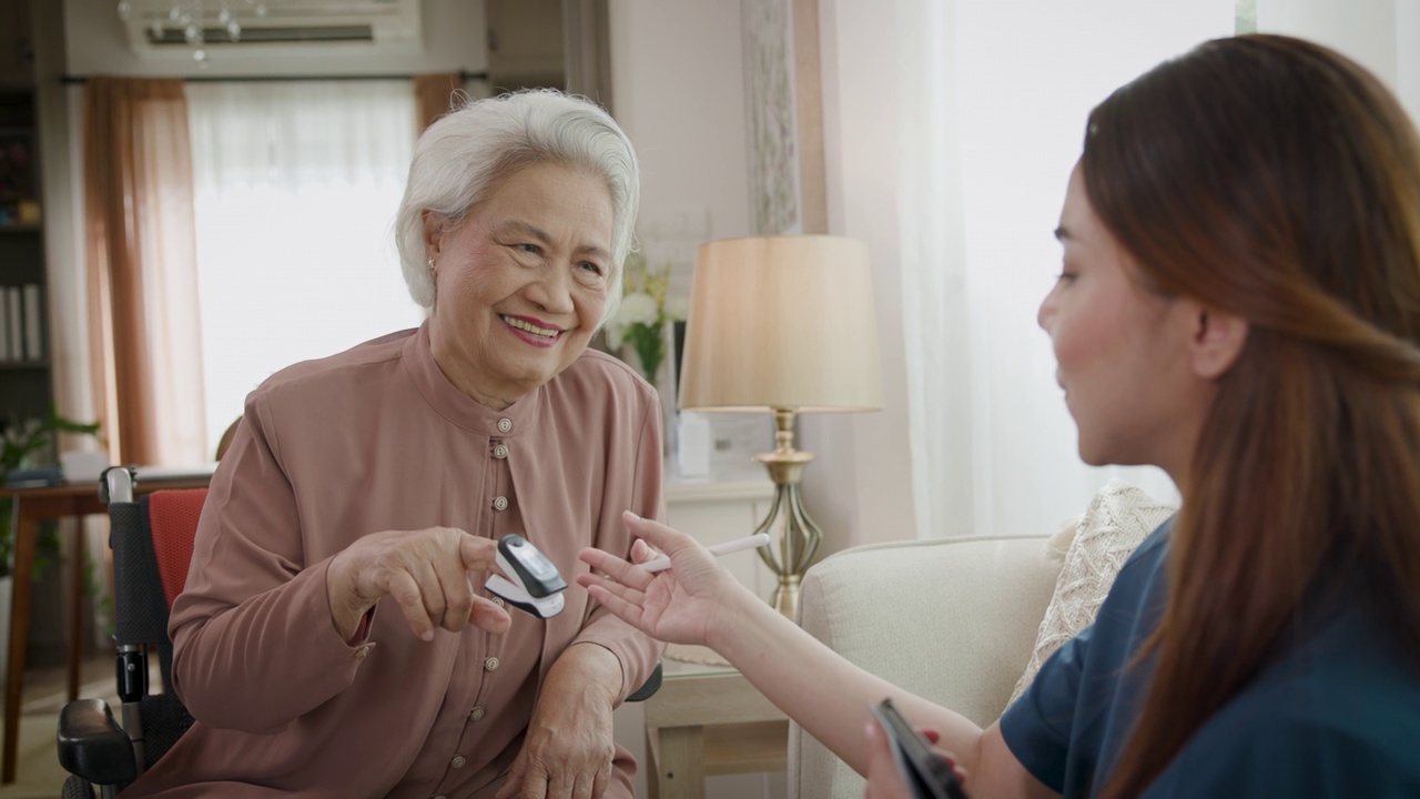 女医生使用血压计和脉搏血氧仪测量血氧饱和度，在诊所或家中与坐在轮椅上的亚洲老年女性患者进行医疗访问视频下载