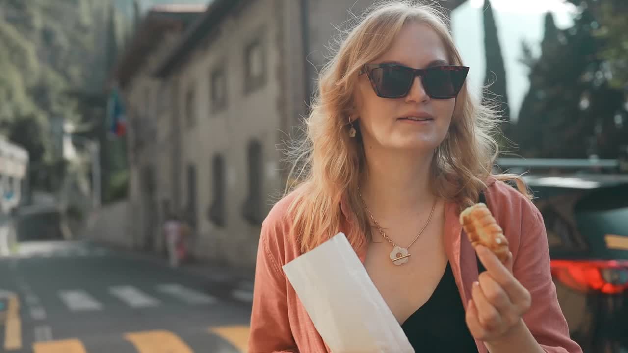 快乐的金发女人吃着传统的柠檬乳清干酪甜卷蛋糕。街头食品视频下载