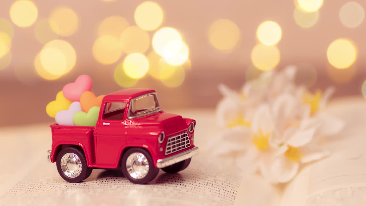 红色的卡车载着五颜六色的心在后面接送情人节的爱情，在模糊的小说书与页展开，散焦的背景光。浪漫的爱情关系视频下载