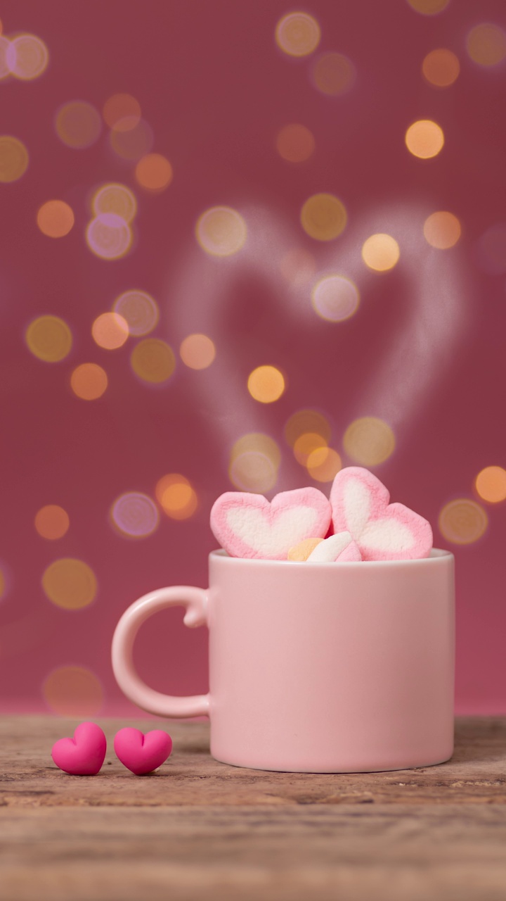 热饮与心形烟在粉红色咖啡杯与心形棉花糖顶部，与两个小心脏并排放置在木桌上，背景散景光。浪漫的爱情关系视频下载