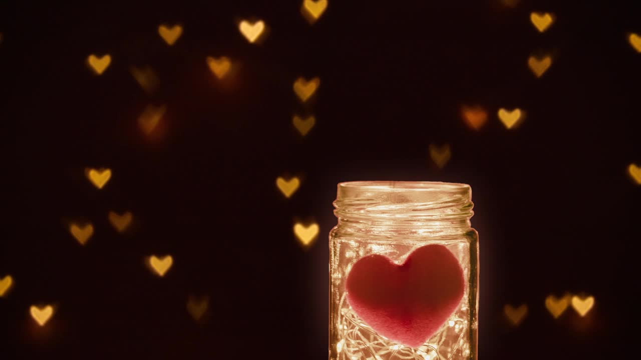 玻璃罐内装有led暖灯和红色的心，在黑暗的背景下闪闪发光，心形散景灯闪闪发光。浪漫爱情关系概念视频下载