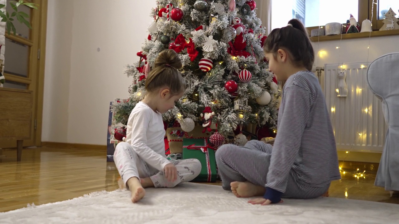 姐妹们穿着睡衣坐在圣诞树旁，打开她们的圣诞礼物视频下载