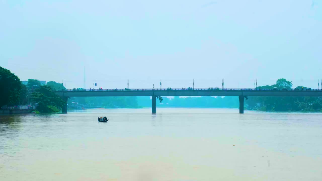 在孟加拉国锡尔赫特，一艘小船在宽阔的河面上行驶，桥下是过往的车流视频下载
