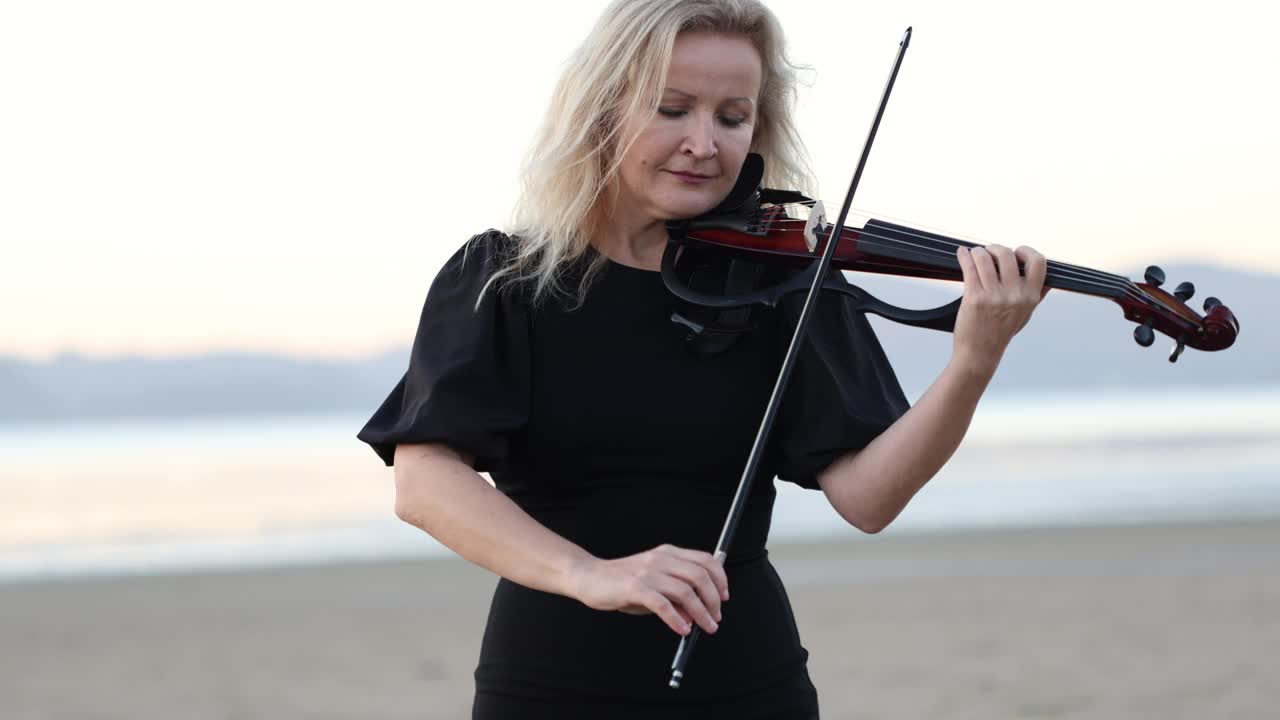 日落时分，金发碧眼的艺术家在海滩上拉小提琴视频下载