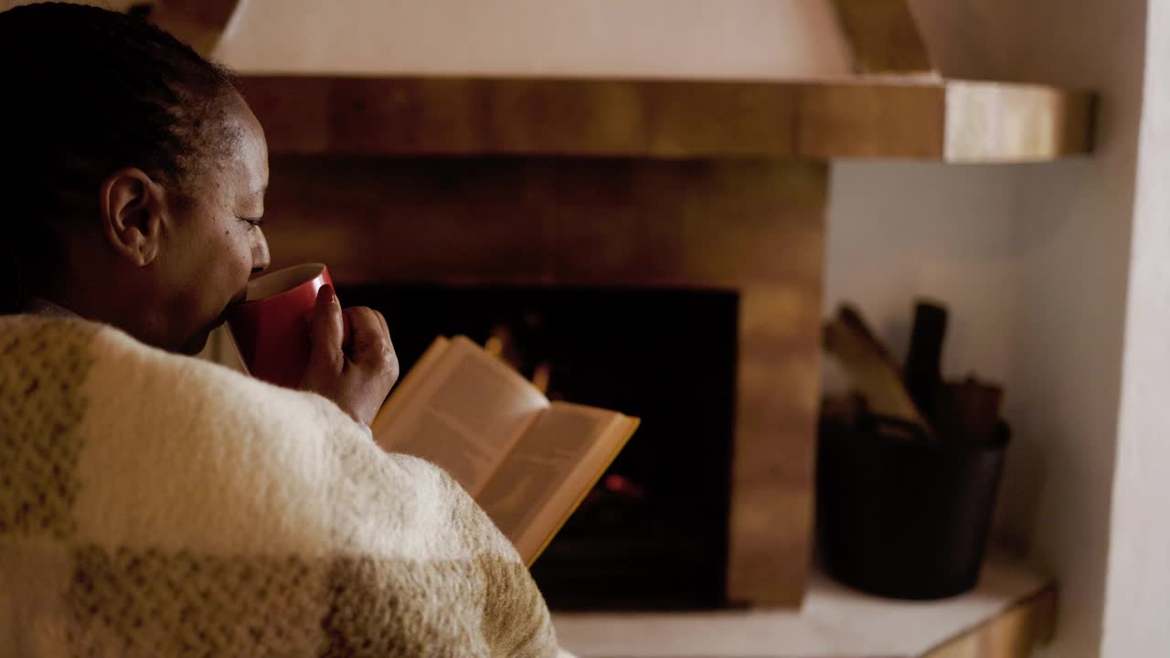 一位年长的非洲妇女在温暖的壁炉边看书。放松休闲活动理念视频下载