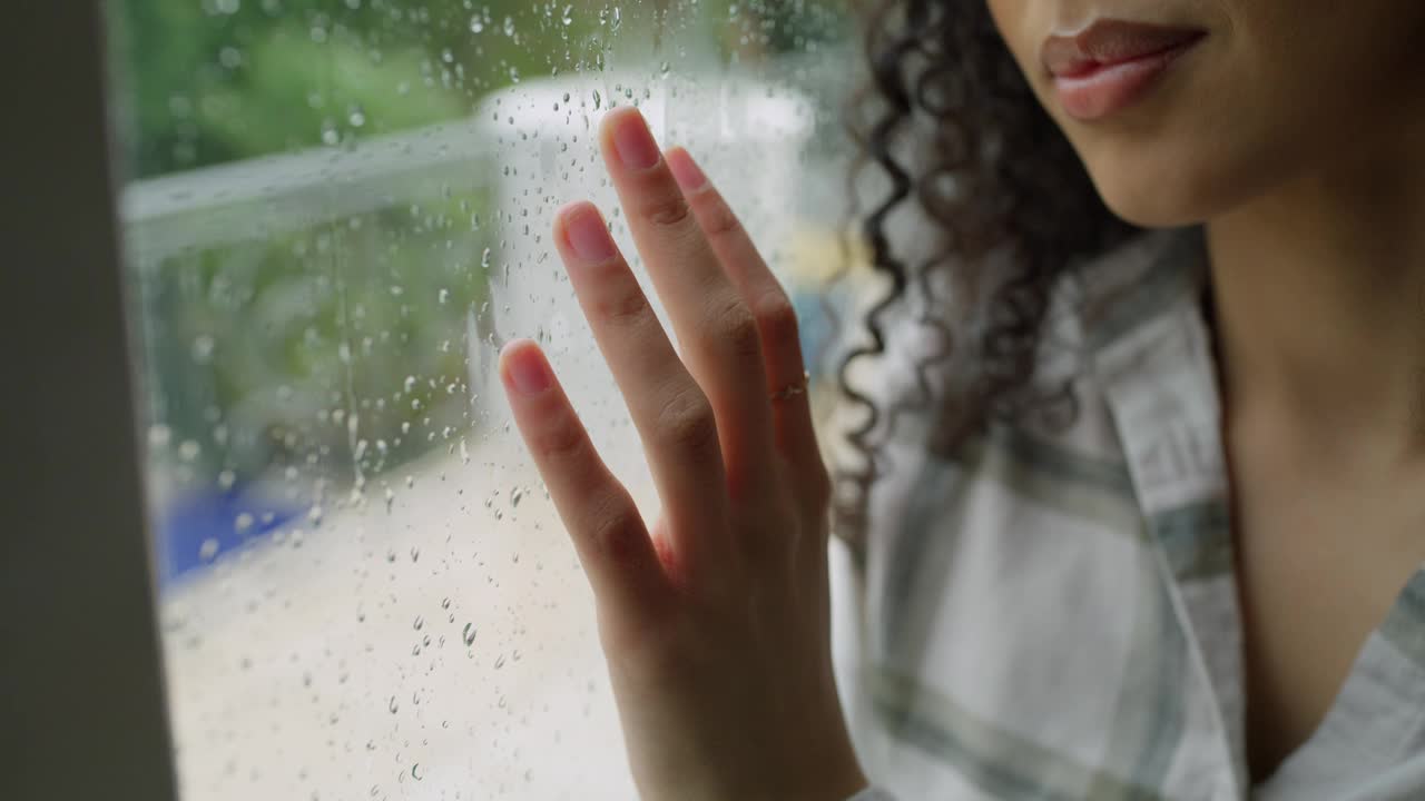 女人，下雨天在窗边手和想，在家里沮丧或紧张。年轻女性在检疫、下雨或家中焦虑时向外看或触摸玻璃框架的特写视频下载