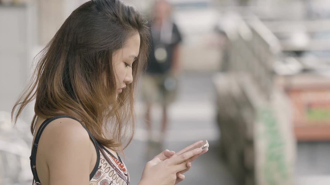 亚洲妇女使用手机的侧面肖像与城市城市背景视频素材